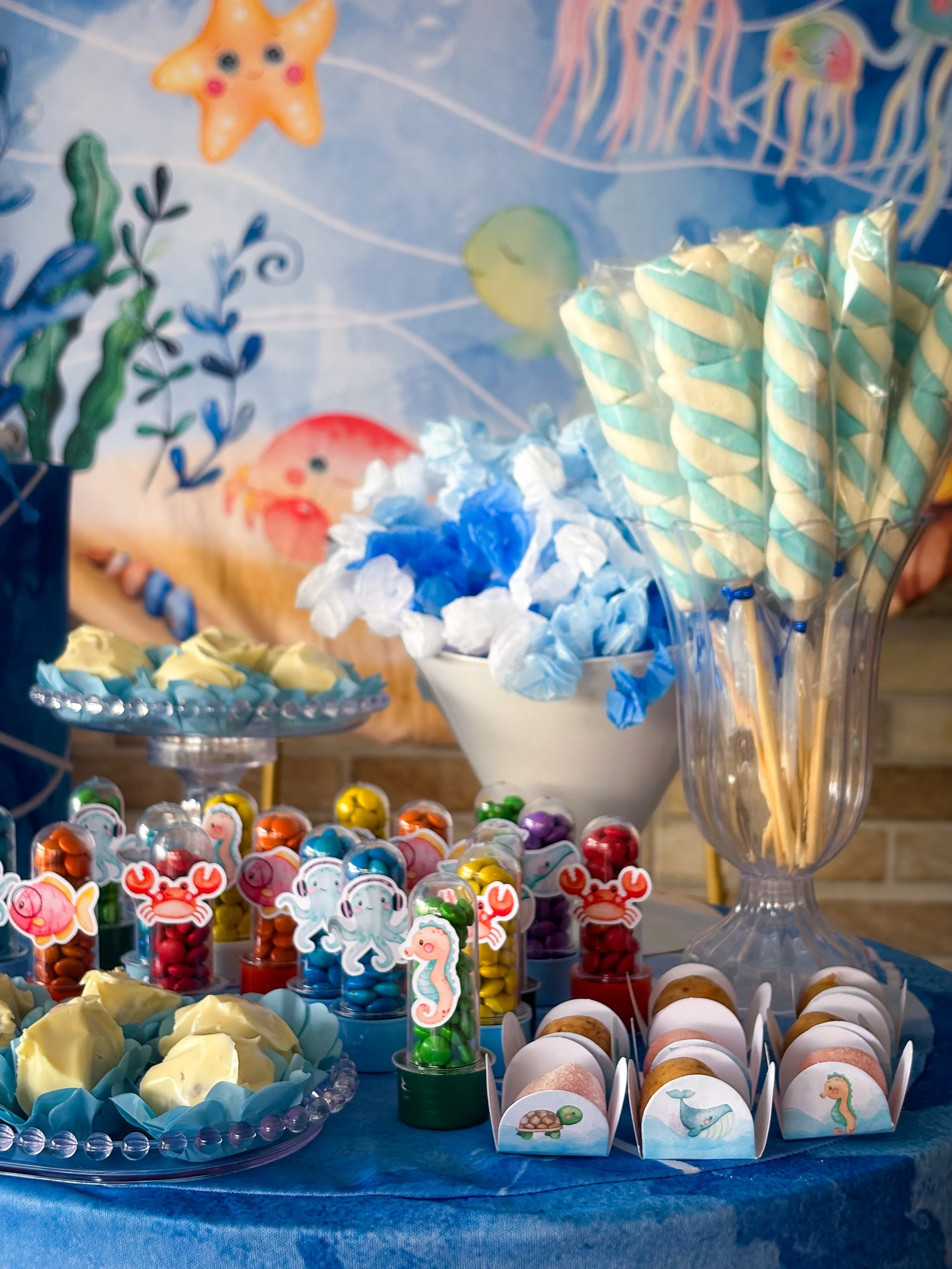 Doces coloridos e canudos listrados em uma mesa decorada com o tema fundo do mar.