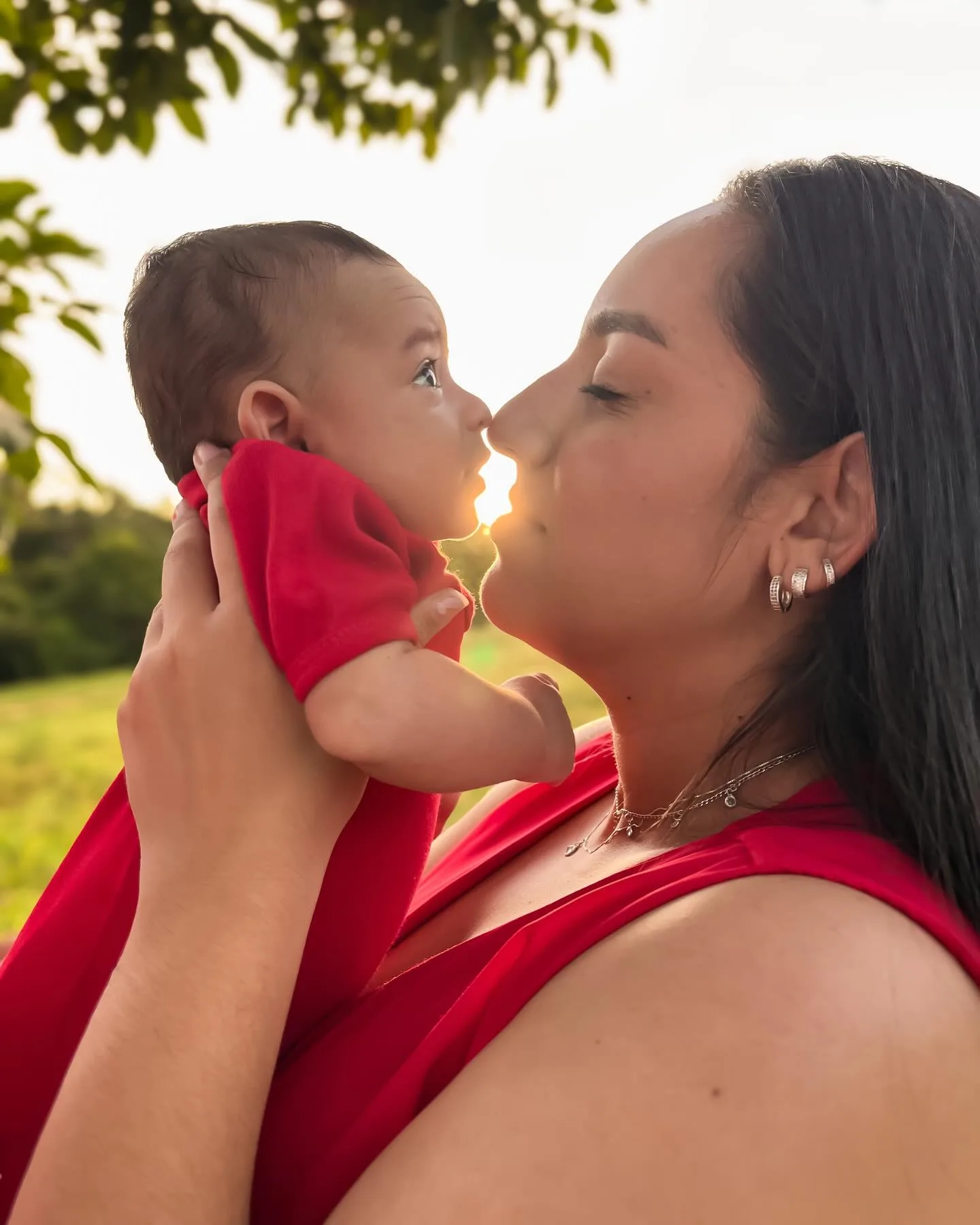 Mulher de vermelho beija um bebê diante da luz do entardecer.