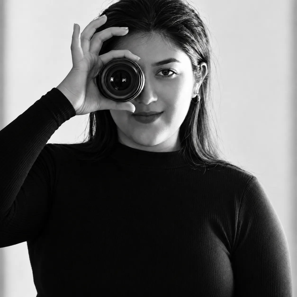 Cinthia Eduarda em retrato preto e branco, segurando uma câmera diante de um dos olhos.