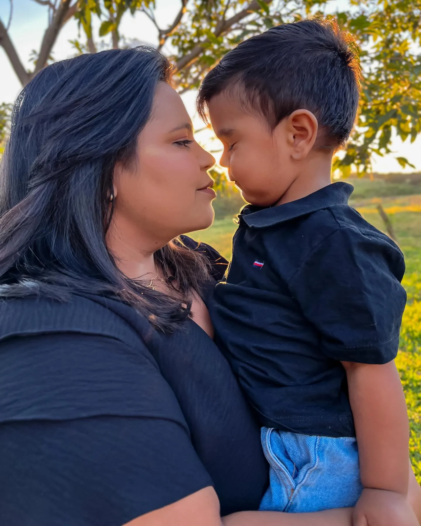 Mulher e menino de camisa escura encostam a testa em um jardim.