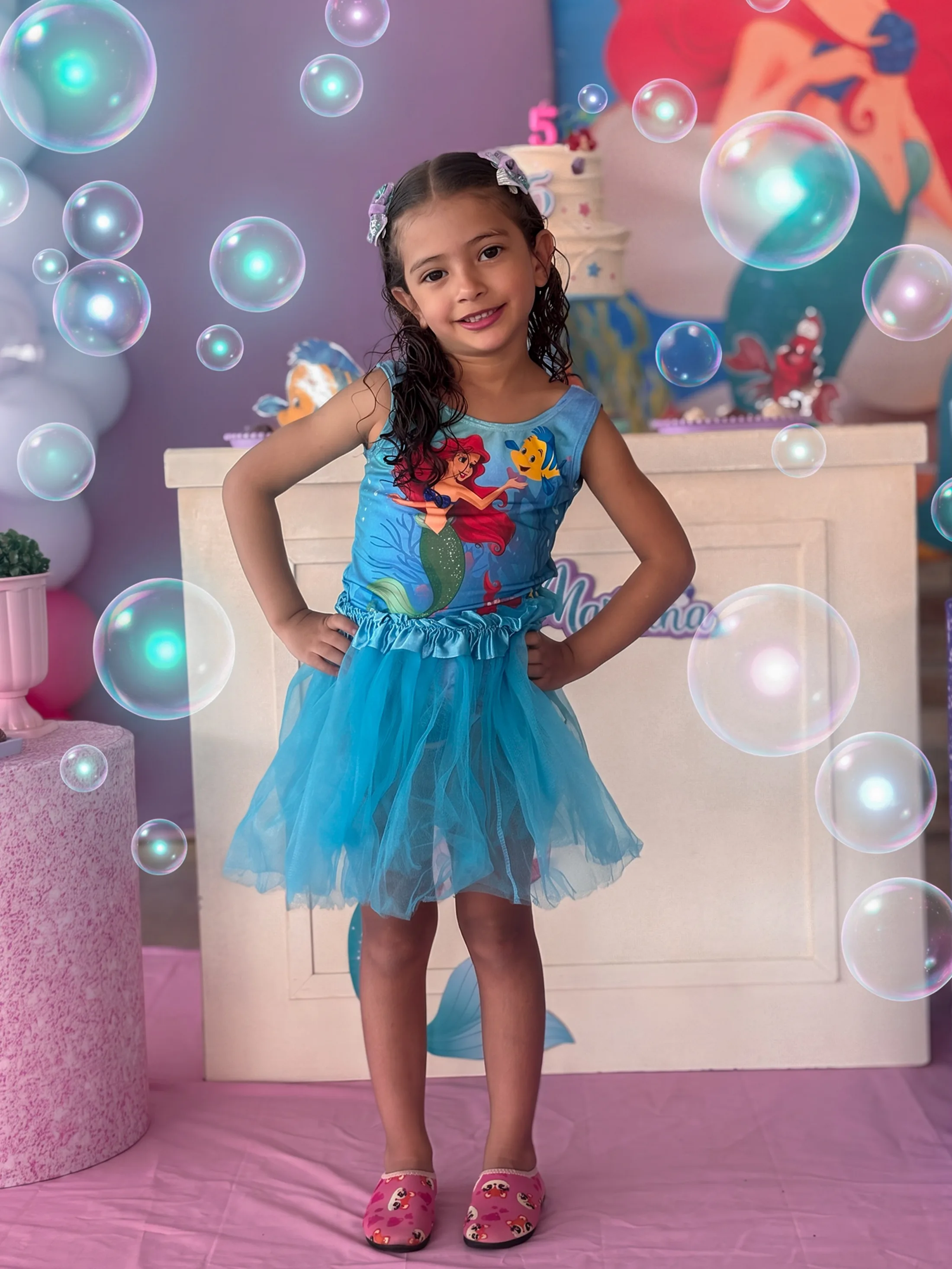 Menina de vestido azul posa diante de uma decoração colorida com balões e personagens.