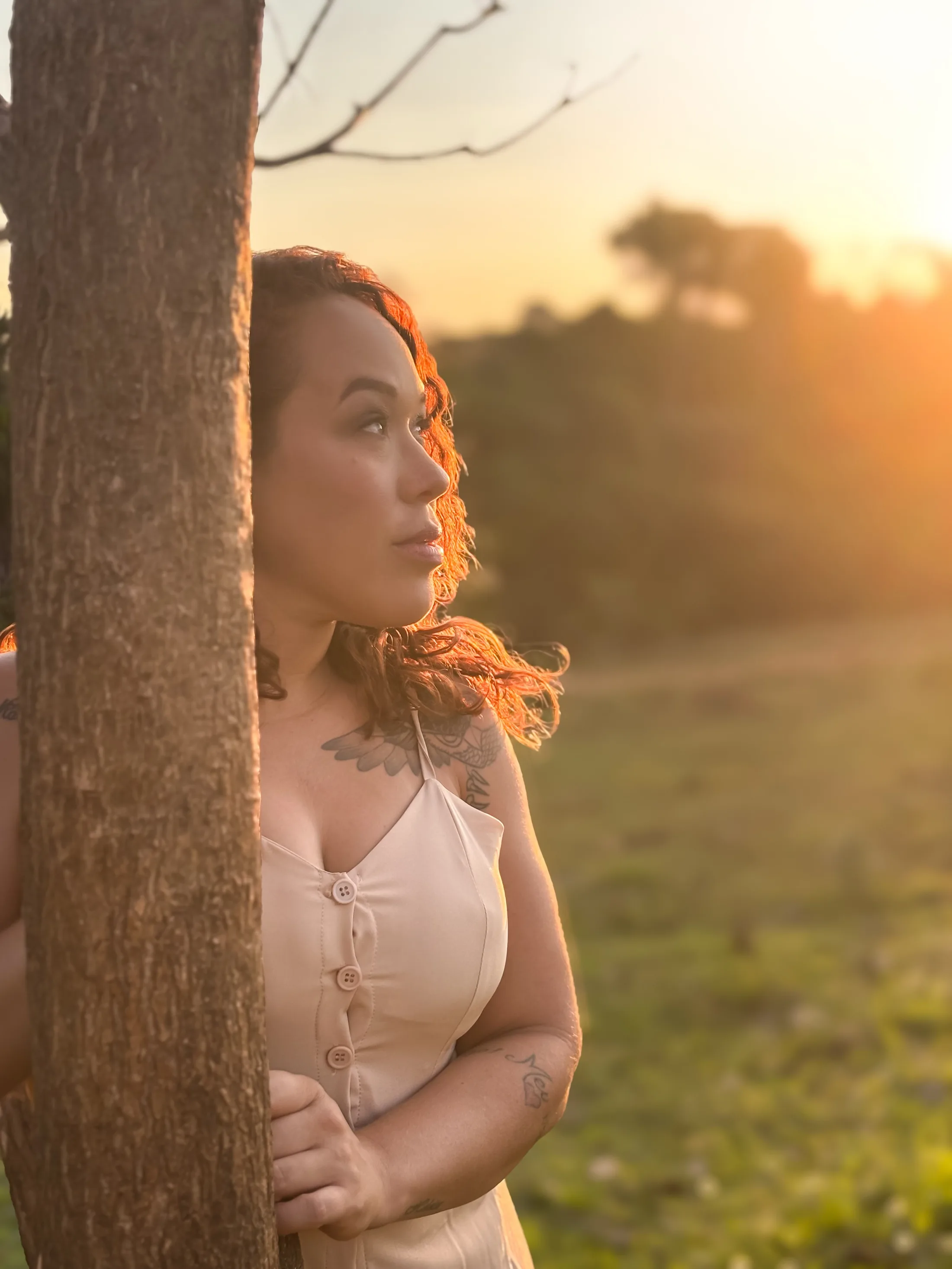 Retrato de mulher junto a um tronco de árvore, com o rosto iluminado pela luz do entardecer.