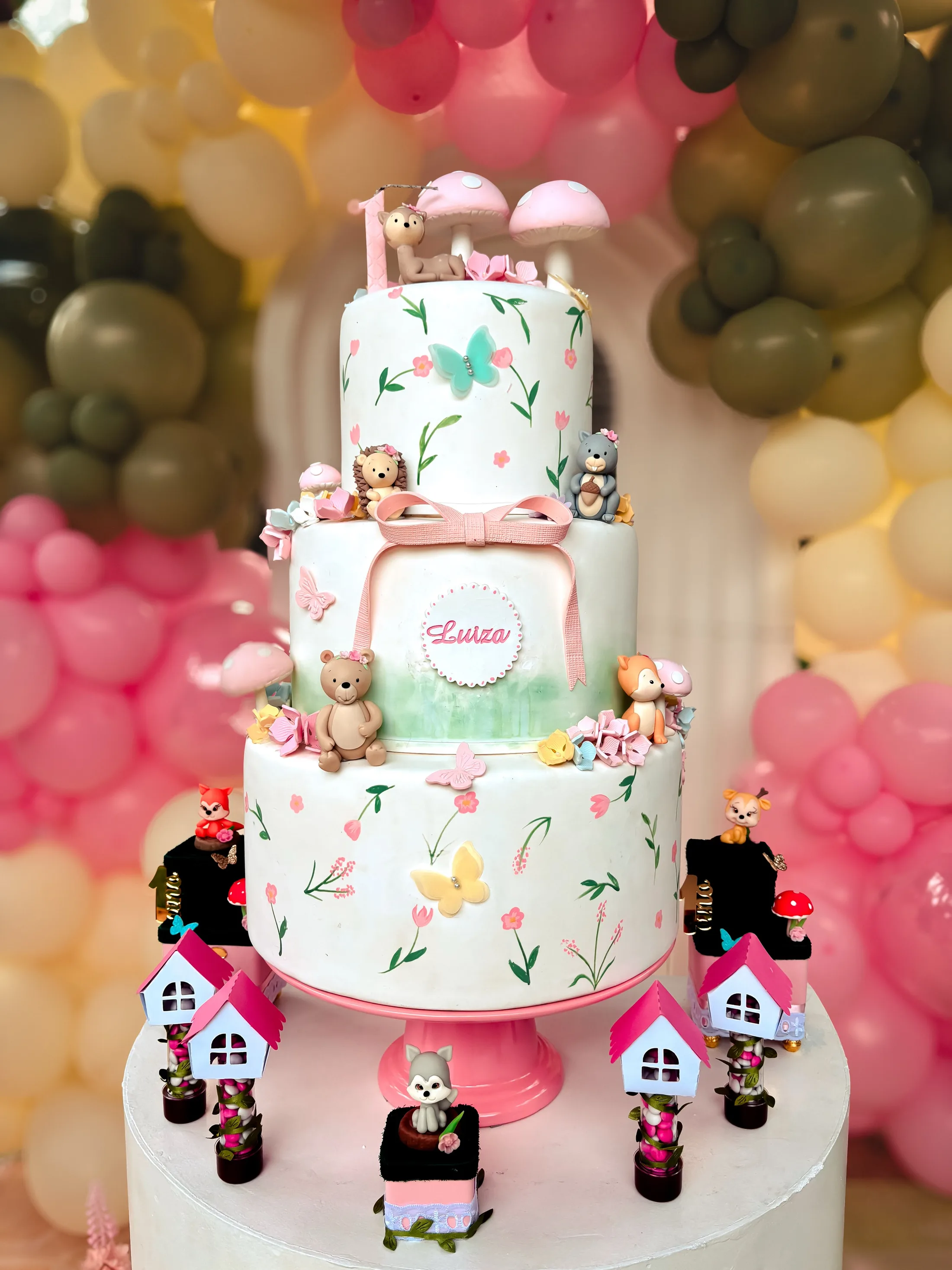 Bolo de andares com flores diante de uma decoração de balões coloridos.