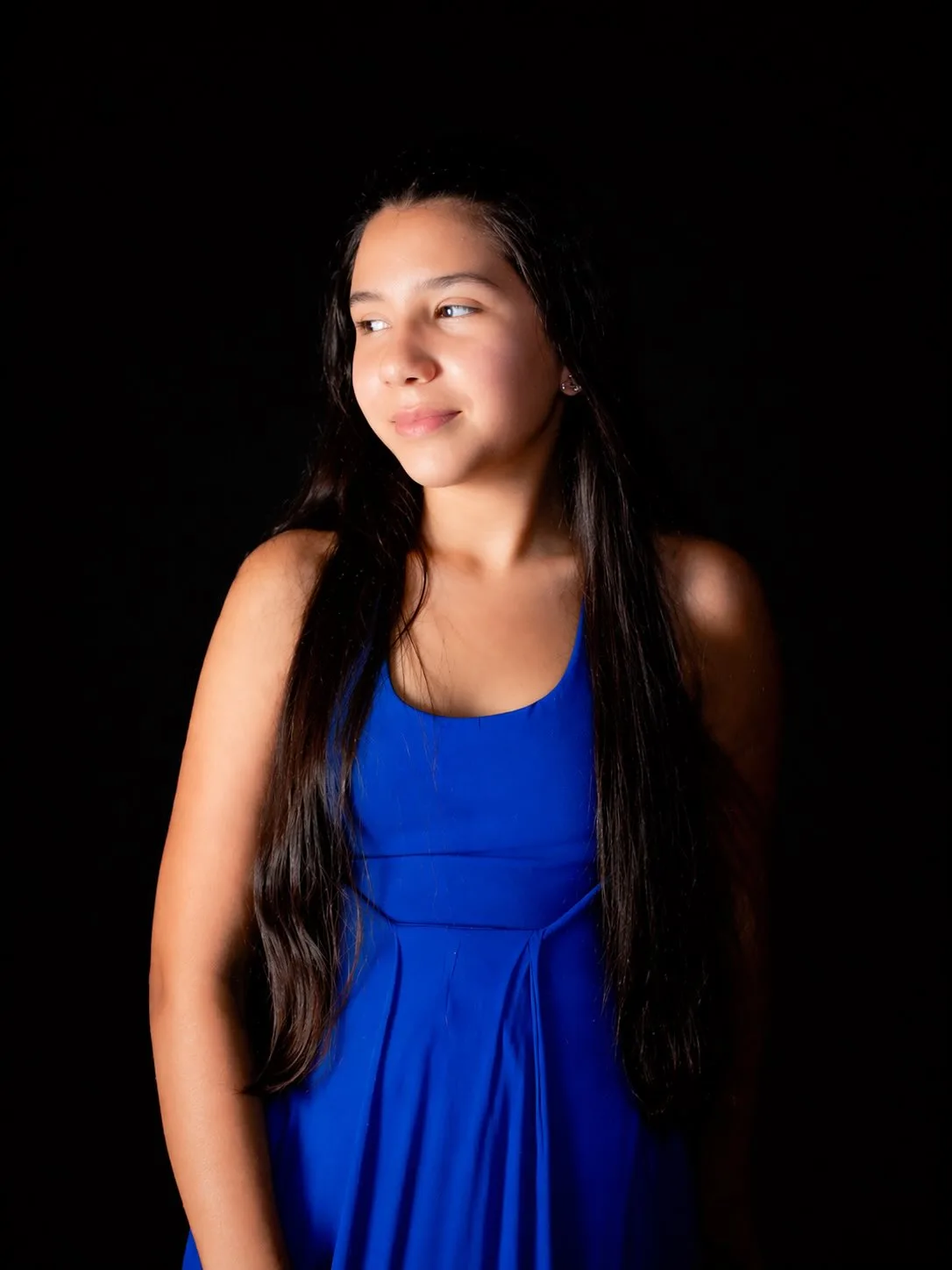 Retrato de mulher de vestido azul iluminada lateralmente diante de fundo preto.