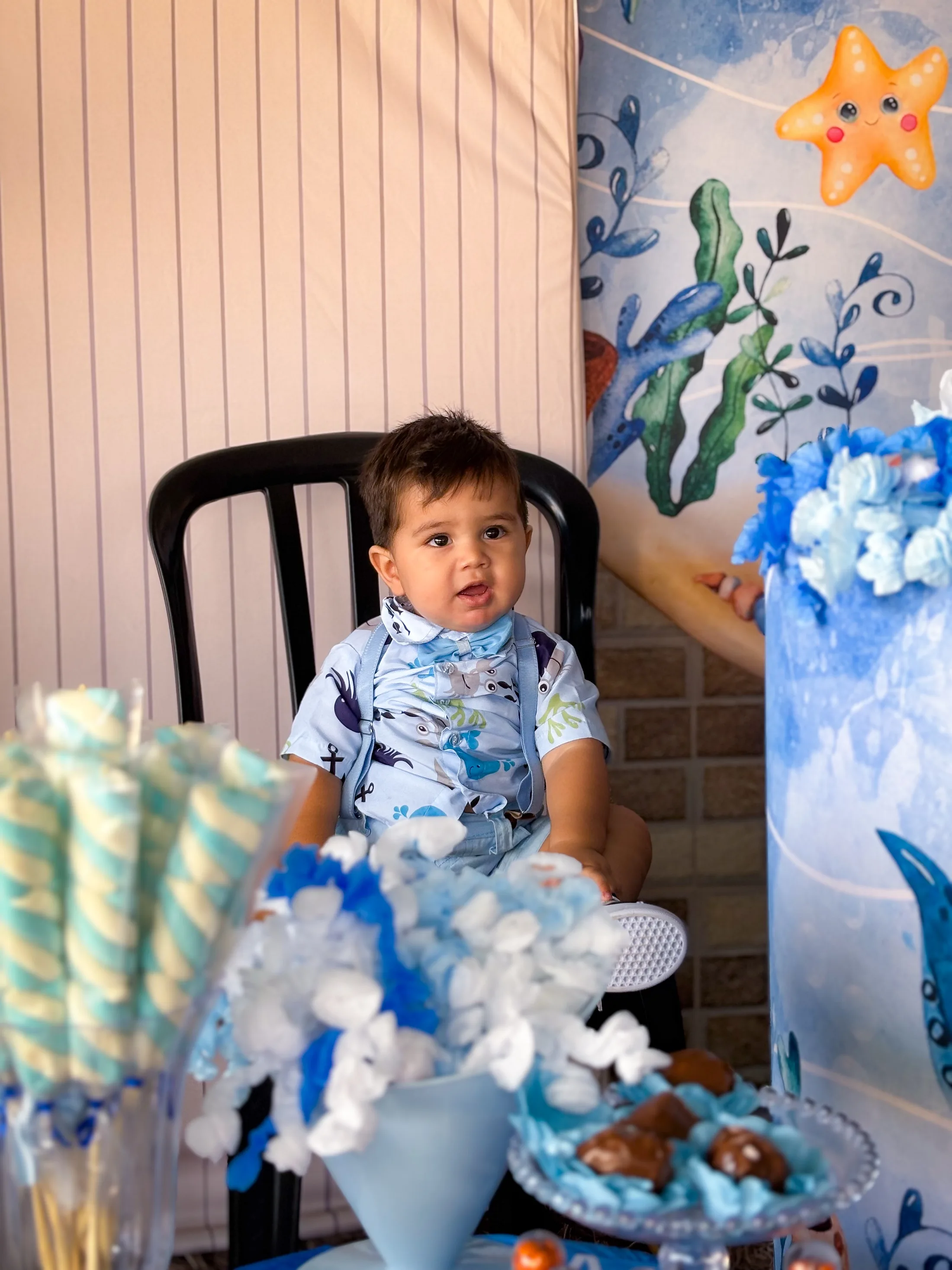 Criança sentada em uma cadeira preta junto a uma mesa com decoração de fundo do mar.