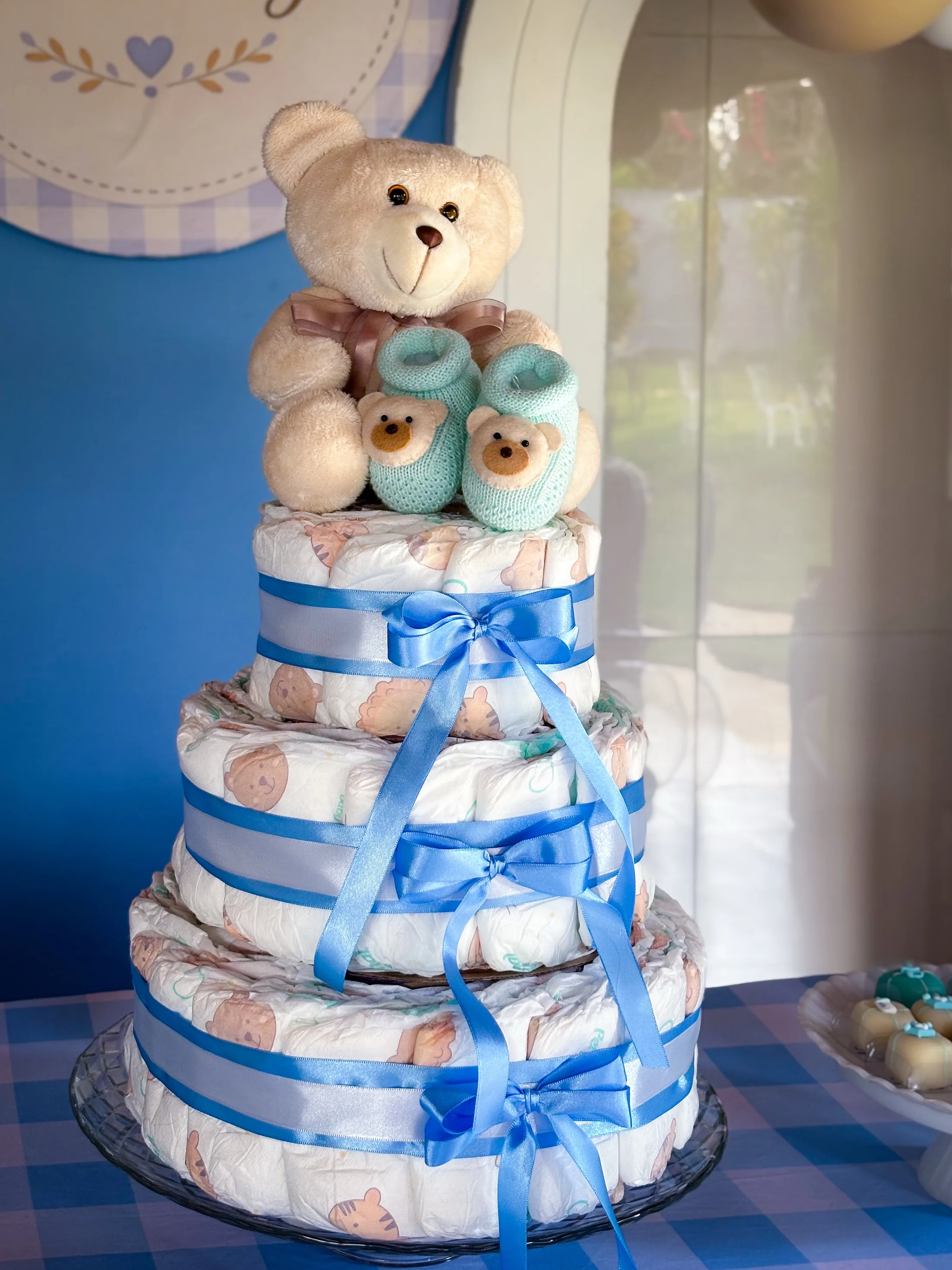 Bolo decorativo azul e branco com um urso de pelúcia no topo.
