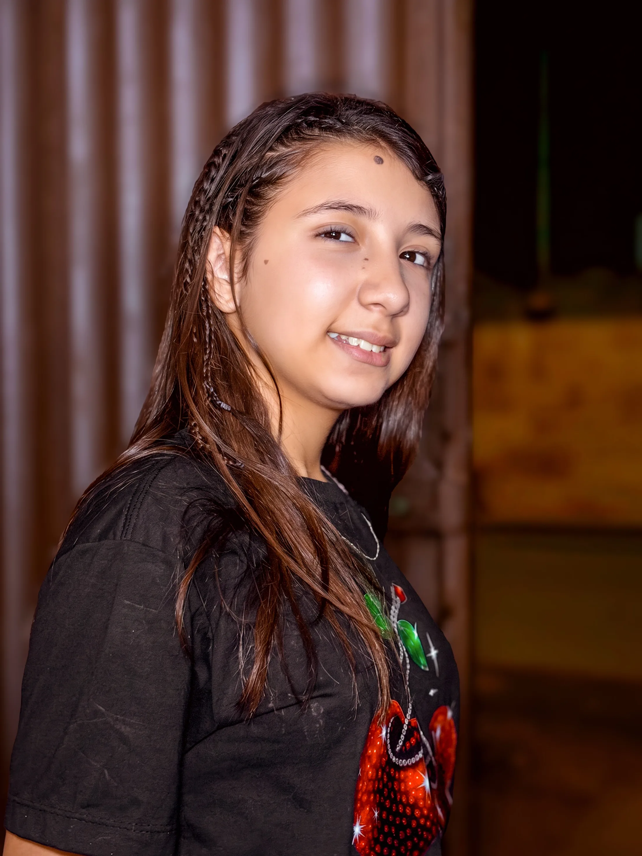 Menina de cabelo molhado sorri diante de uma cortina e um ambiente escuro.