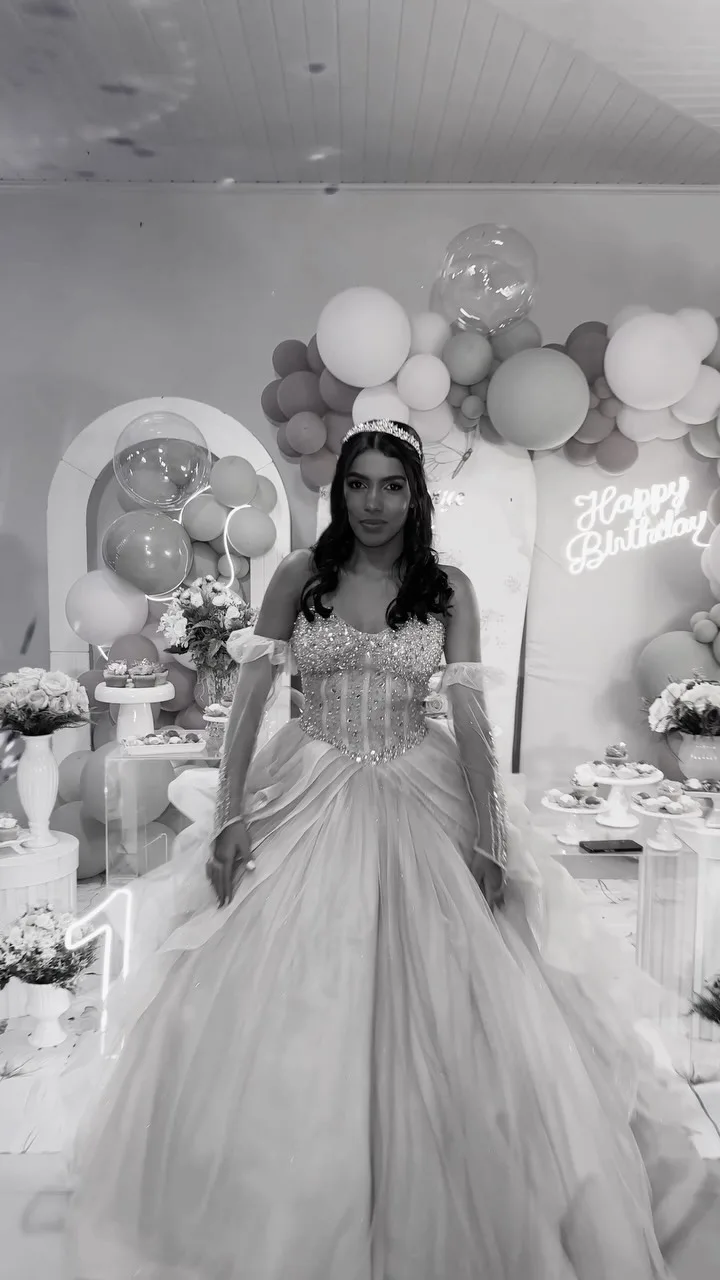 Mulher de vestido longo claro diante de uma decoração com balões, em preto e branco.