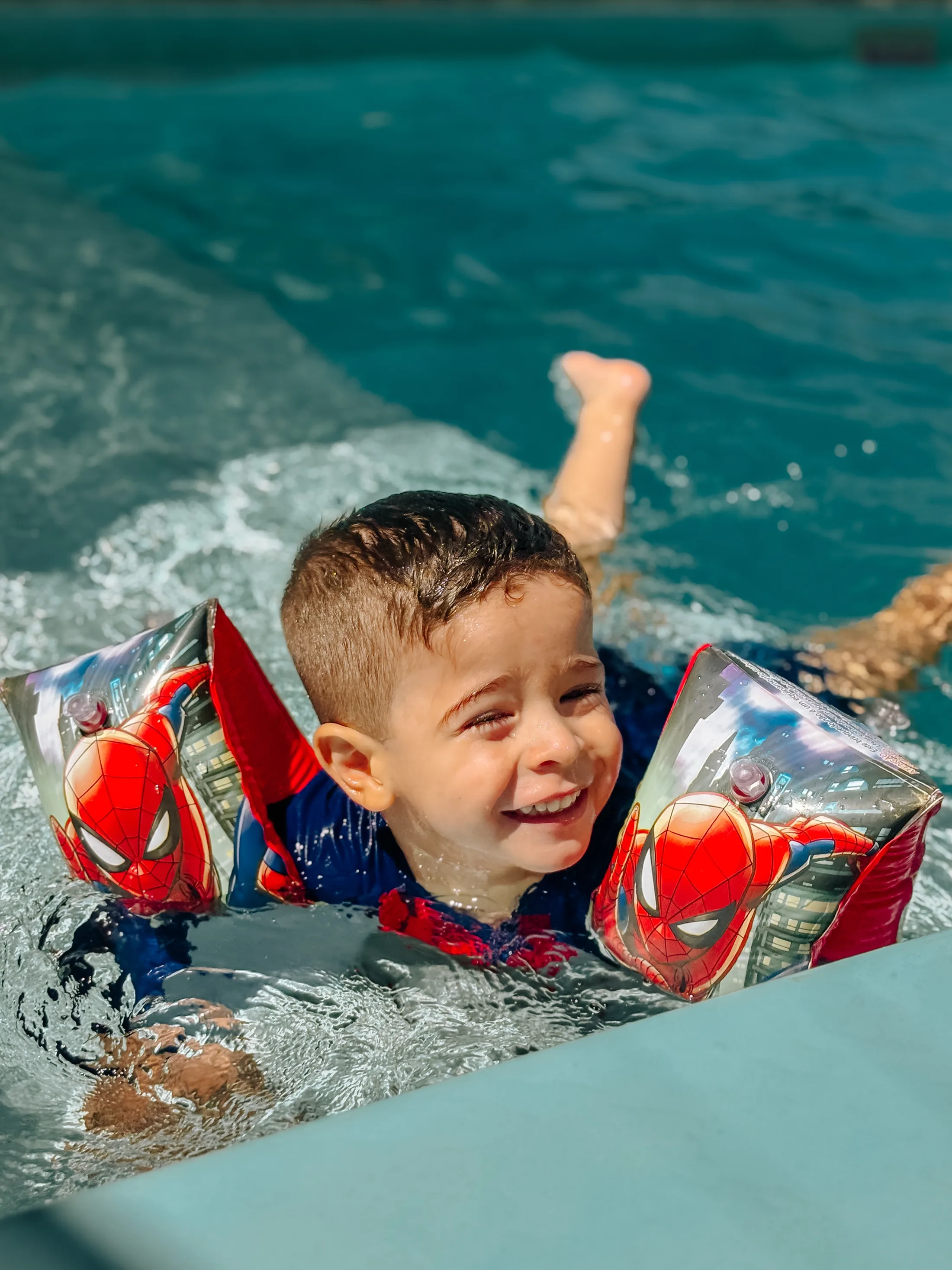 Criança com boias coloridas sorri dentro de uma piscina azul.